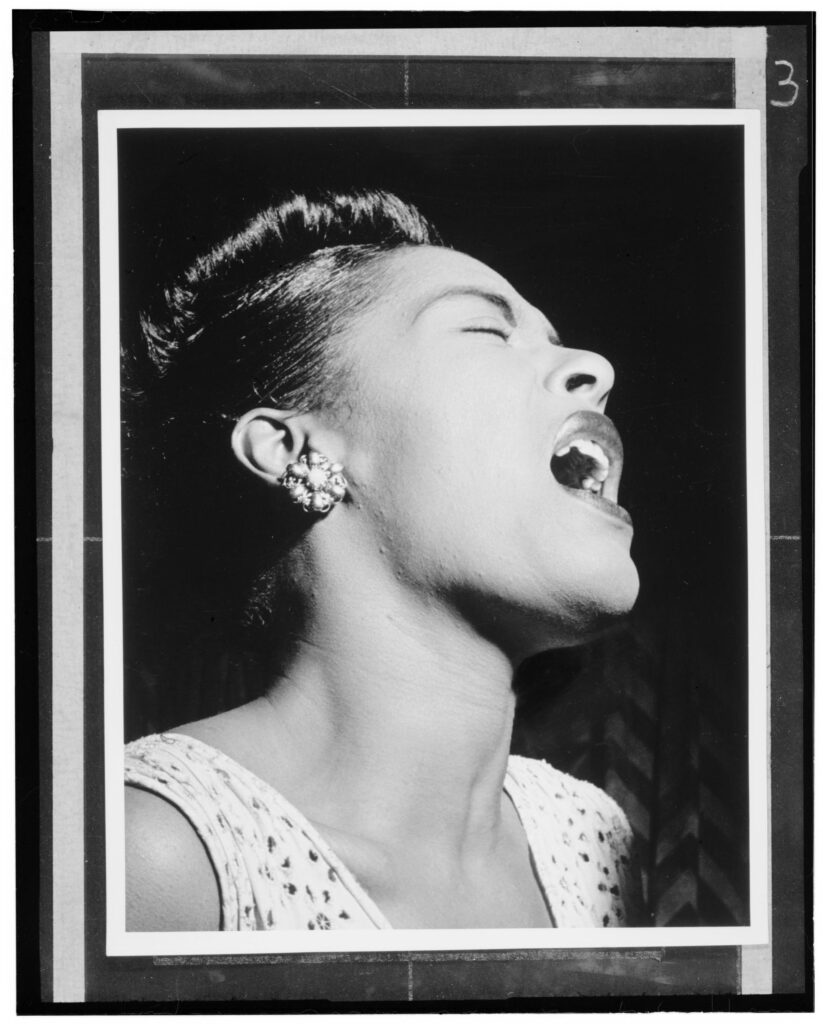 Black-and-white portrait of Billie Holiday singing with her eyes closed, photographed by William P. Gottlieb at the Downbeat in New York
